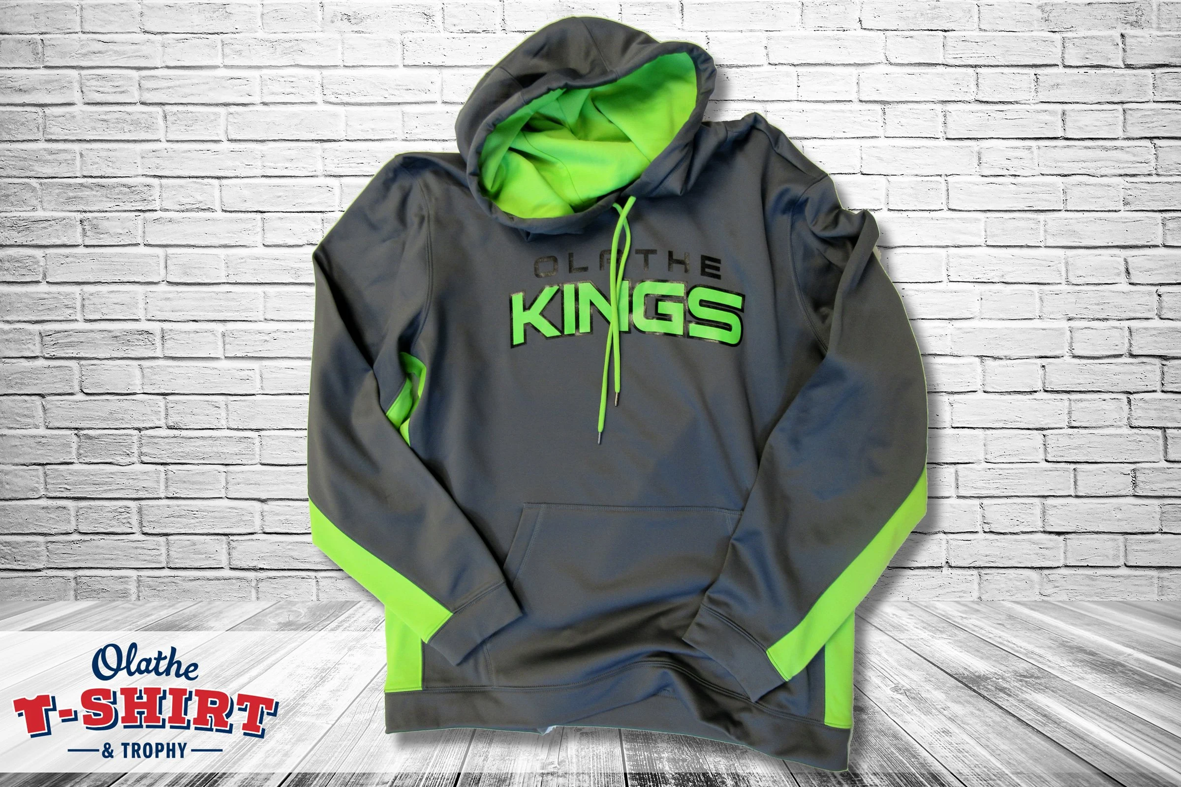 Gray hoodie with neon green interior and accents hanging against a white brick wall.
