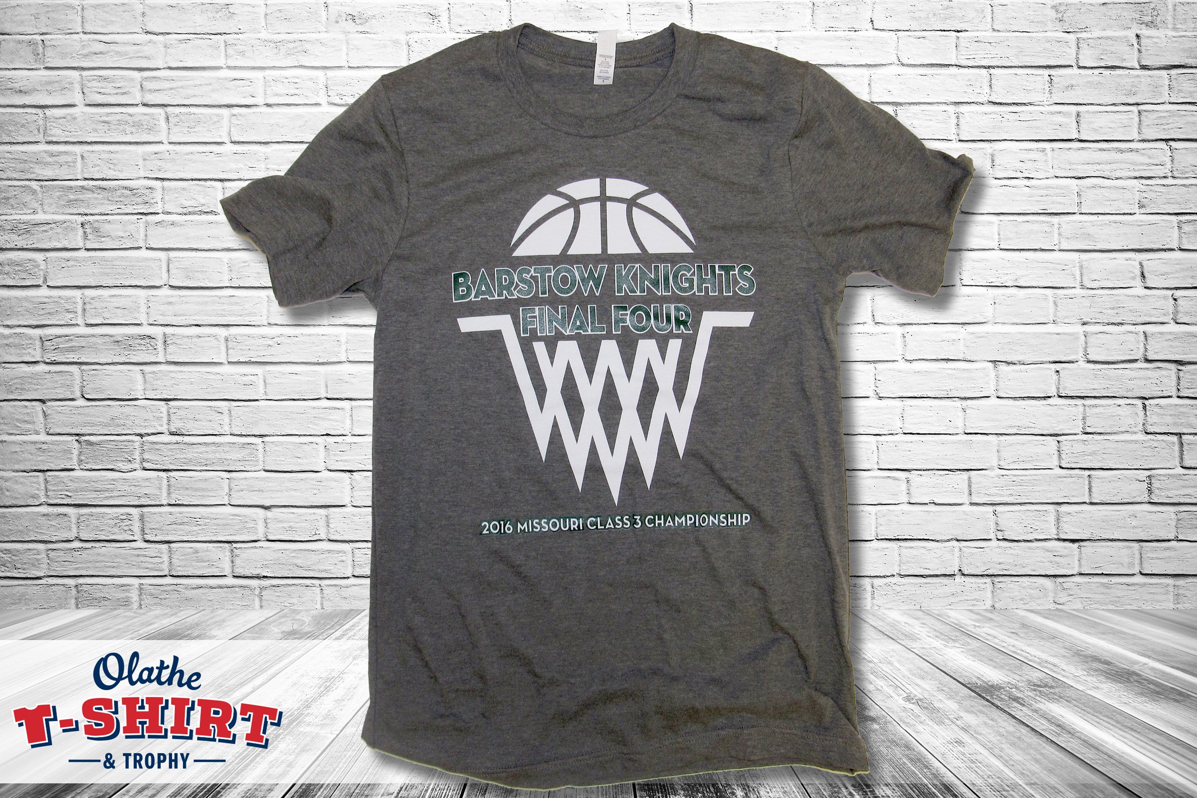 Gray basketball championship shirt with green, white and black graphics.