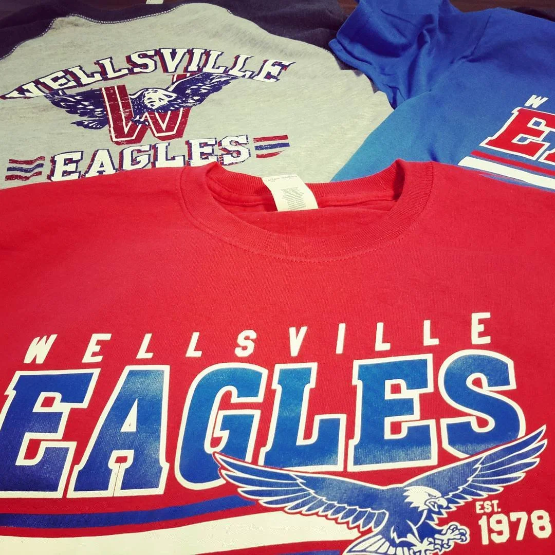 Red Eagles shirt with a mascot graphic, displayed with coordinating blue and gray shirts.