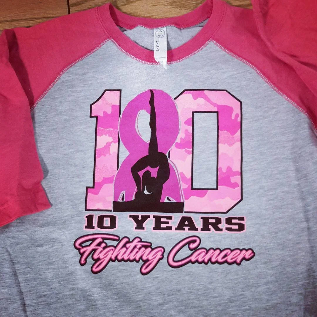 Gray and pink long-sleeve shirt with a large anniversary number and pink camouflage details.