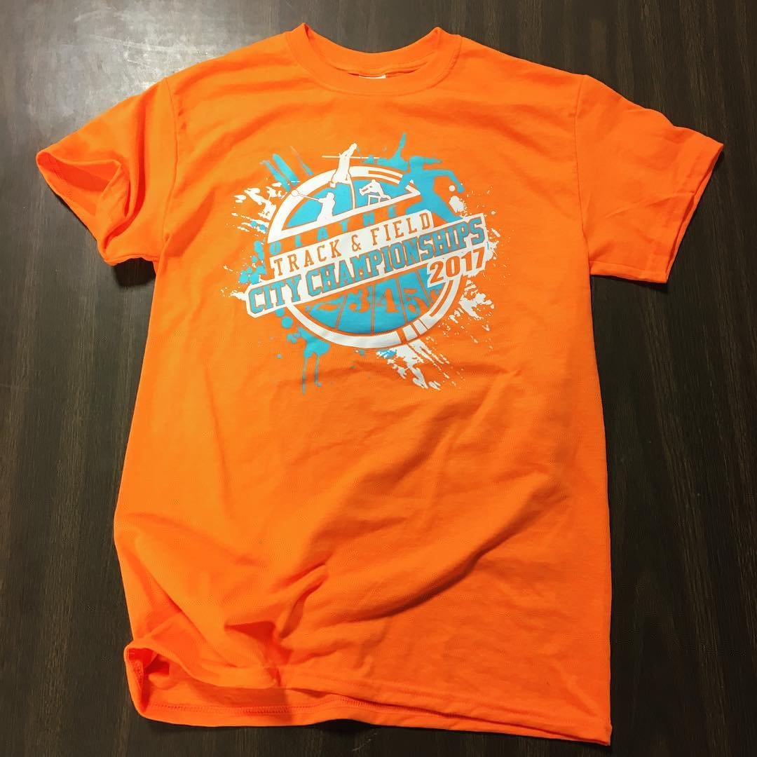 Orange T-shirt with a graphic design for the 2017 Atlanta Track & Field City Championships, featuring images of track and field athletes, a mile marker, and a same sweeping splash design.