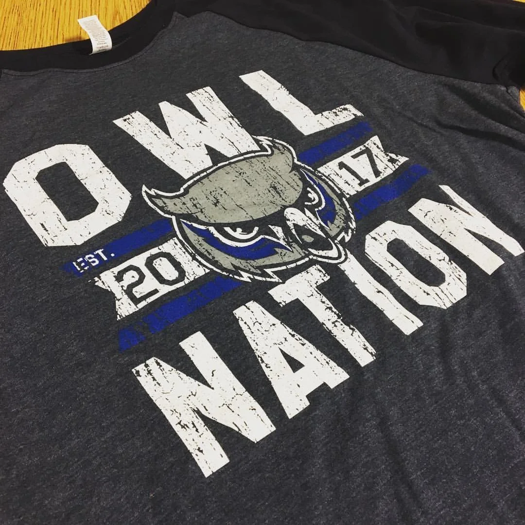 Dark gray T-shirt with a mascot graphic and blue and white lettering.