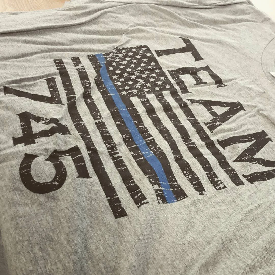 Gray T-shirt with a distressed design of a police badge featuring the American flag with a blue line, and the words 'TEAM K-9'.