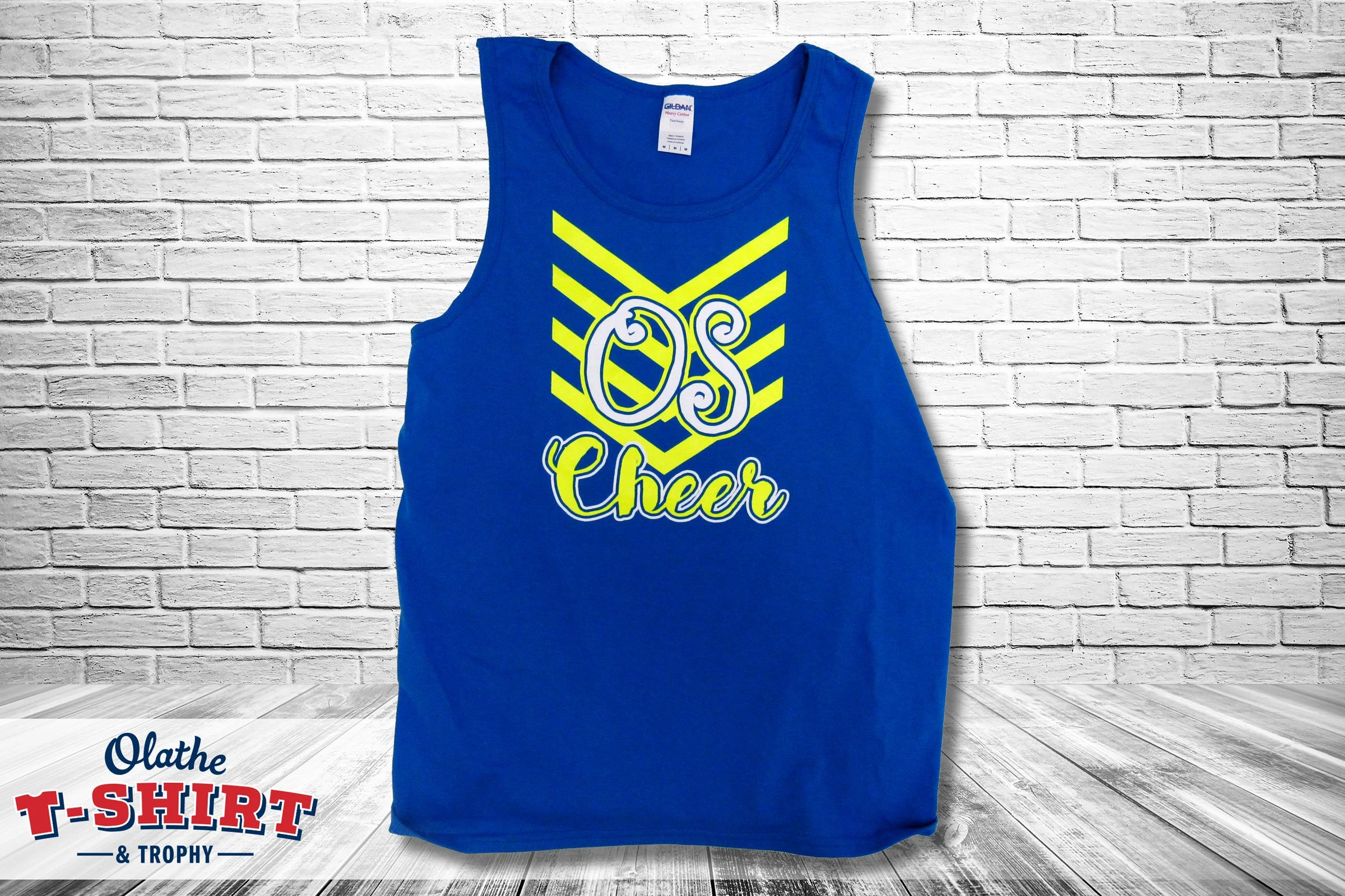 Blue cheerleading tank top with a yellow and white graphic design on the front, displayed against a white brick wall background.