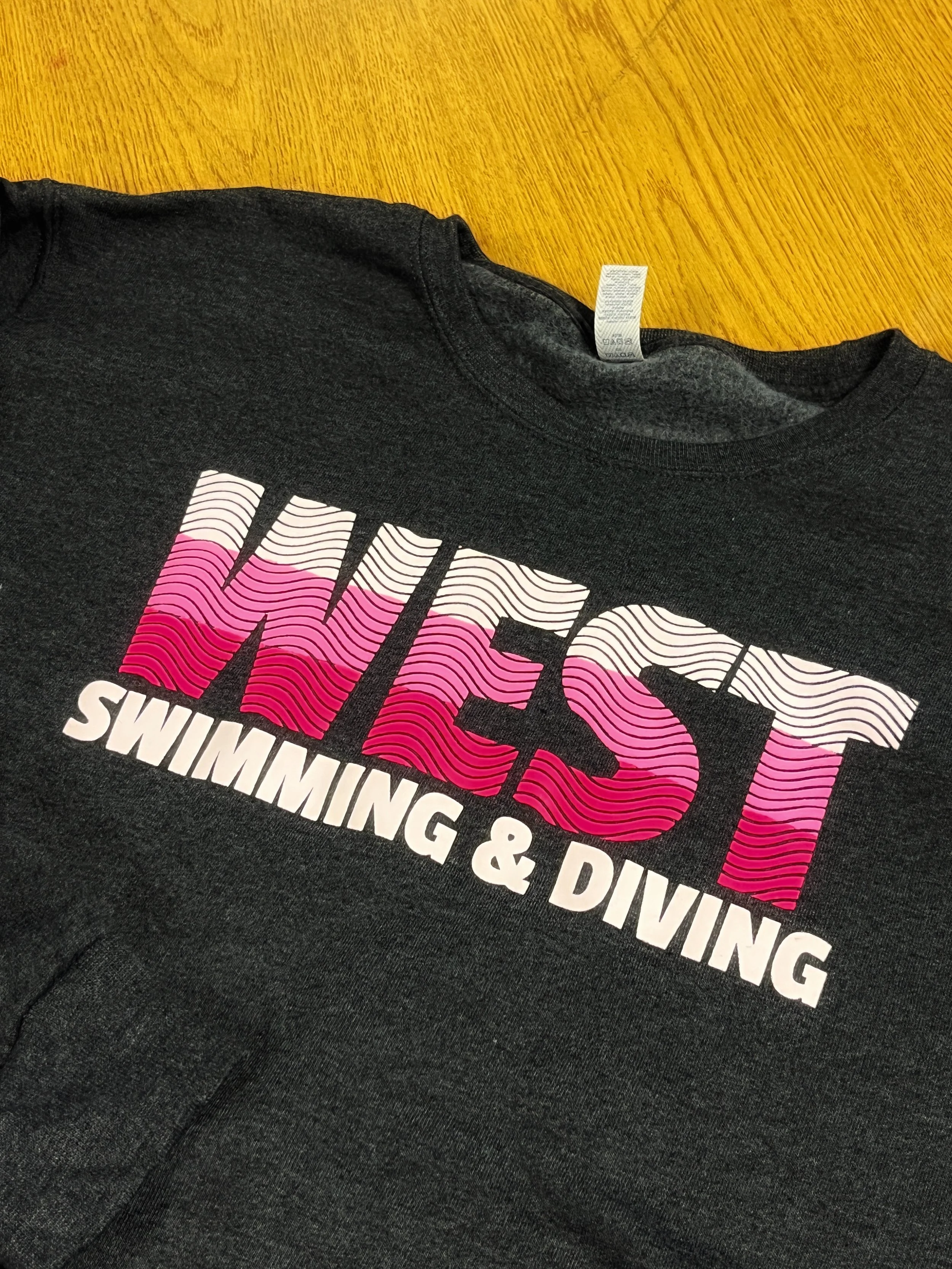 Close-up of a black t-shirt with pink and white text, laying on a wooden surface.
