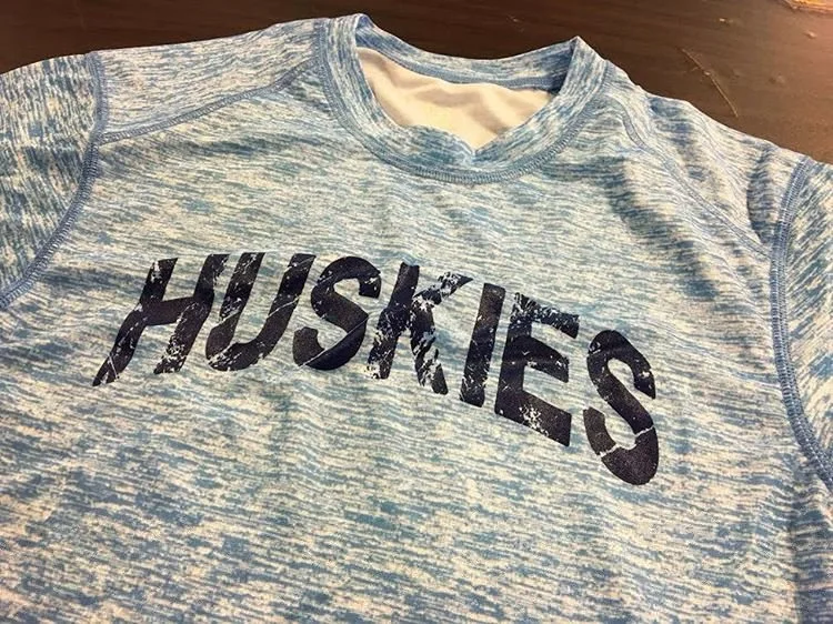 A light blue athletic shirt with the word 'HUSKIES' printed in large, distressed black letters