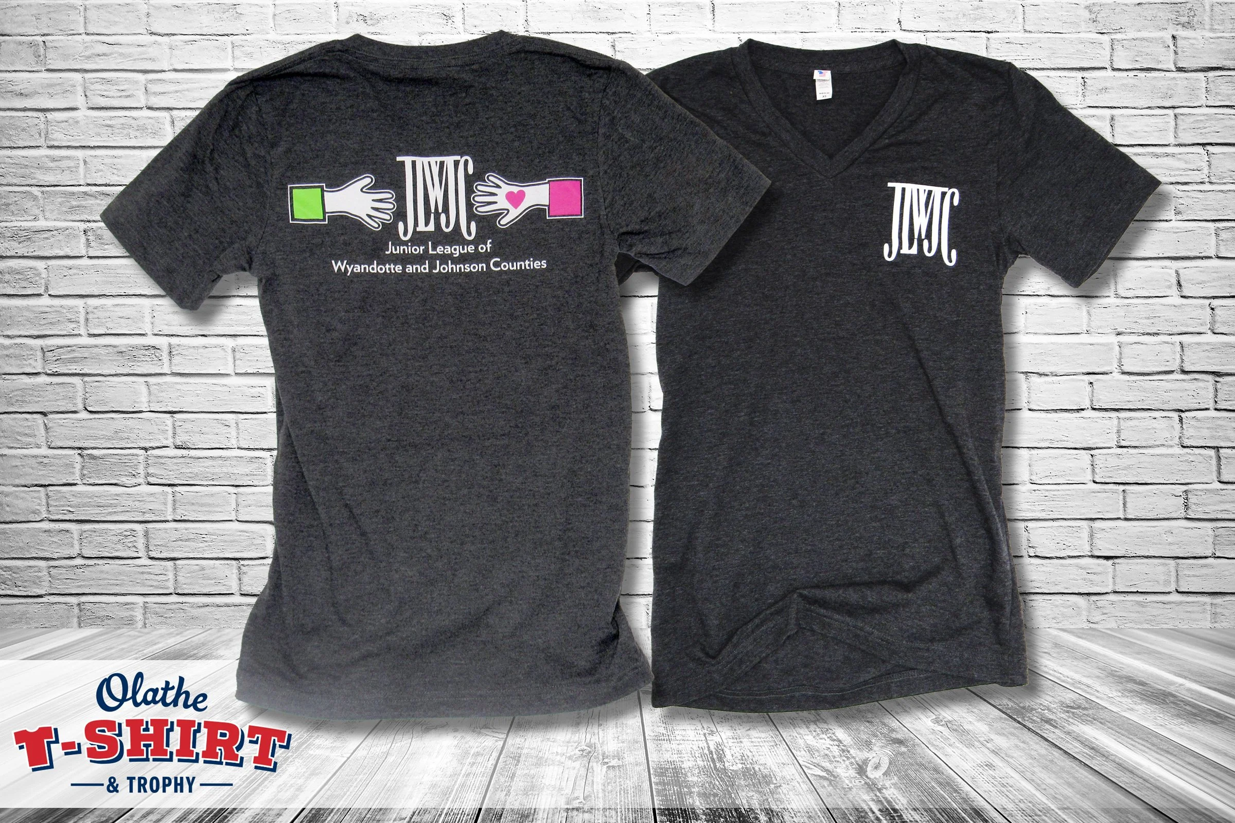Front and back of dark gray Junior League shirts with hands, a heart and organization lettering.