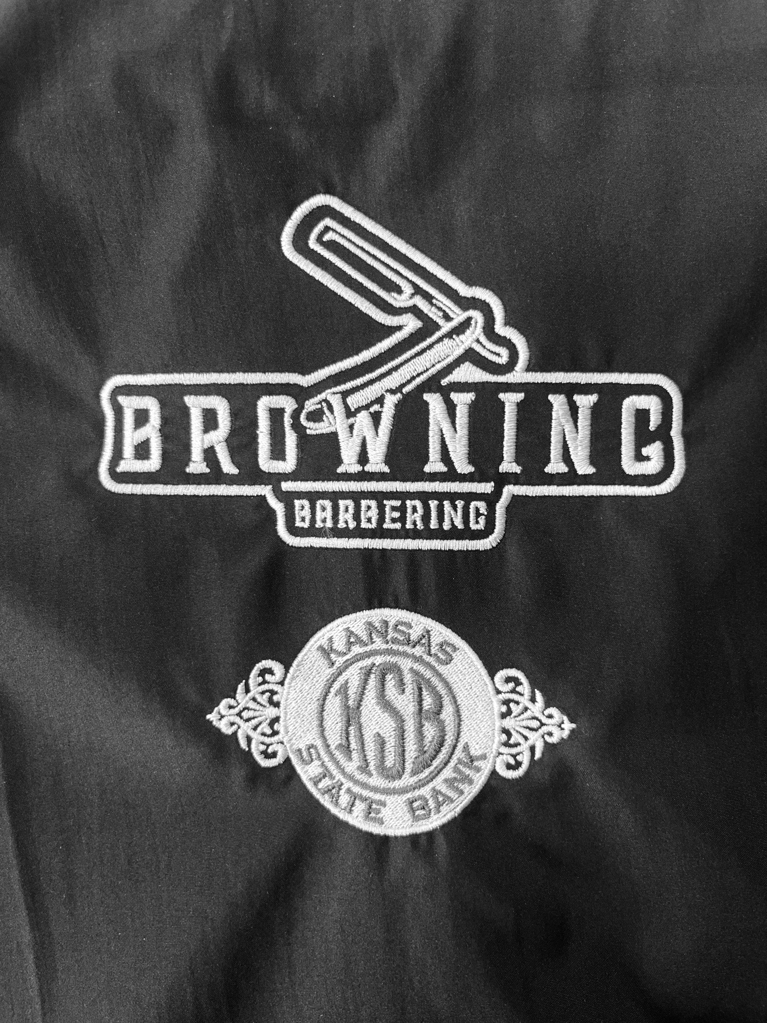 Barber-shop name and straight-razor graphic embroidered on dark fabric.