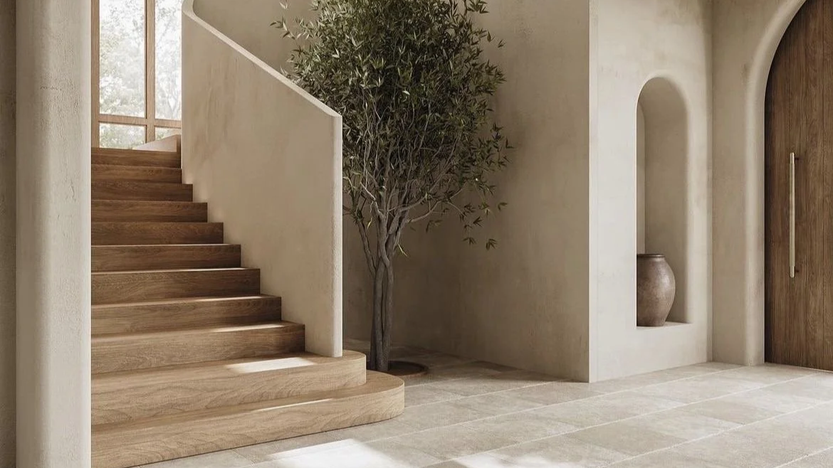 Interior view of a modern home with wooden stairs, a potted tree, a built-in nook with a vase, and a wooden arched door.