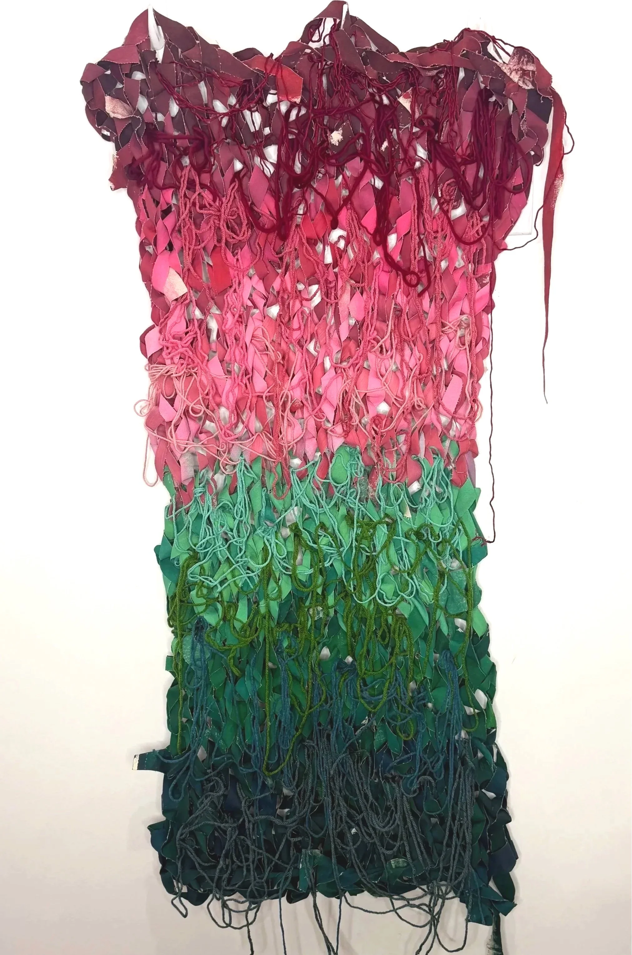 A pink and purple textured, layered art piece hanging on a white wall, resembling an abstract floral or organic shape.