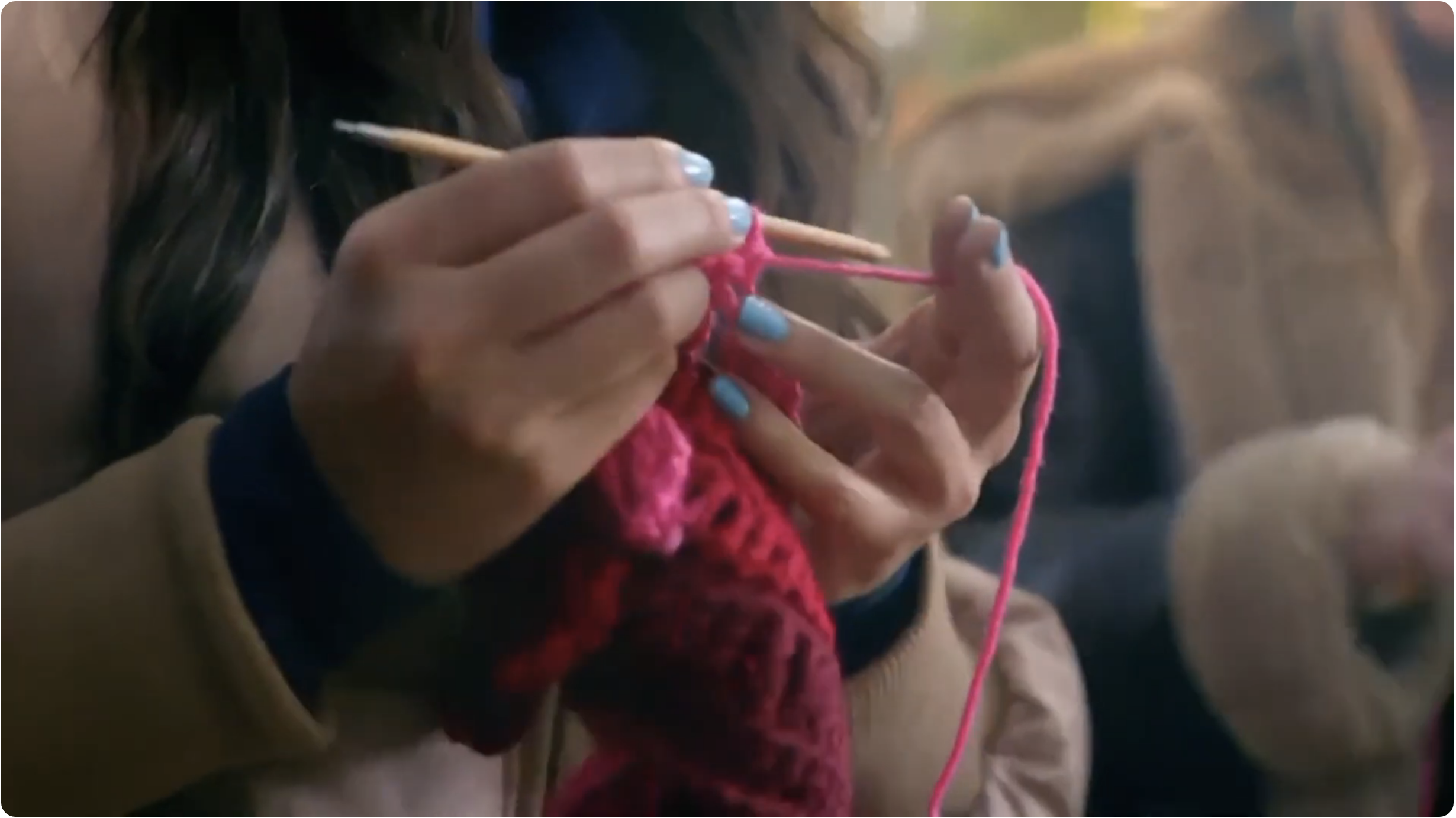 Close-up of hands knitting with pink yarn using wooden knitting needles.