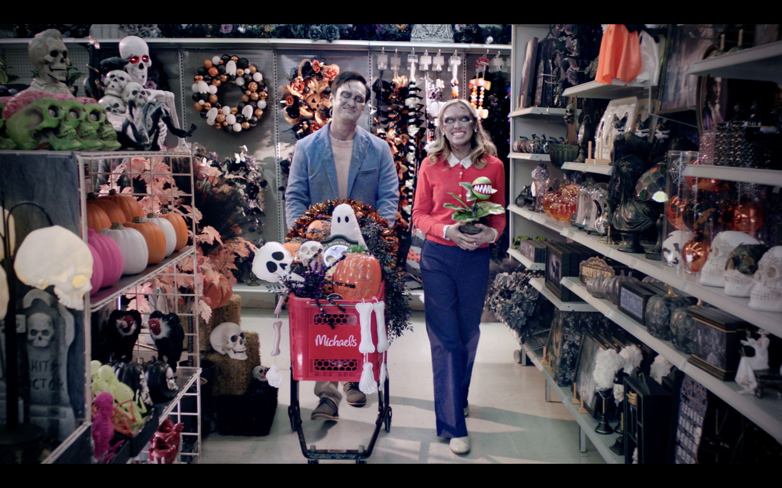 People dressed as skeletons and ghouls shopping for Halloween decorations at a craft store, with shelves of skulls, pumpkins, and Halloween-themed ornaments.
