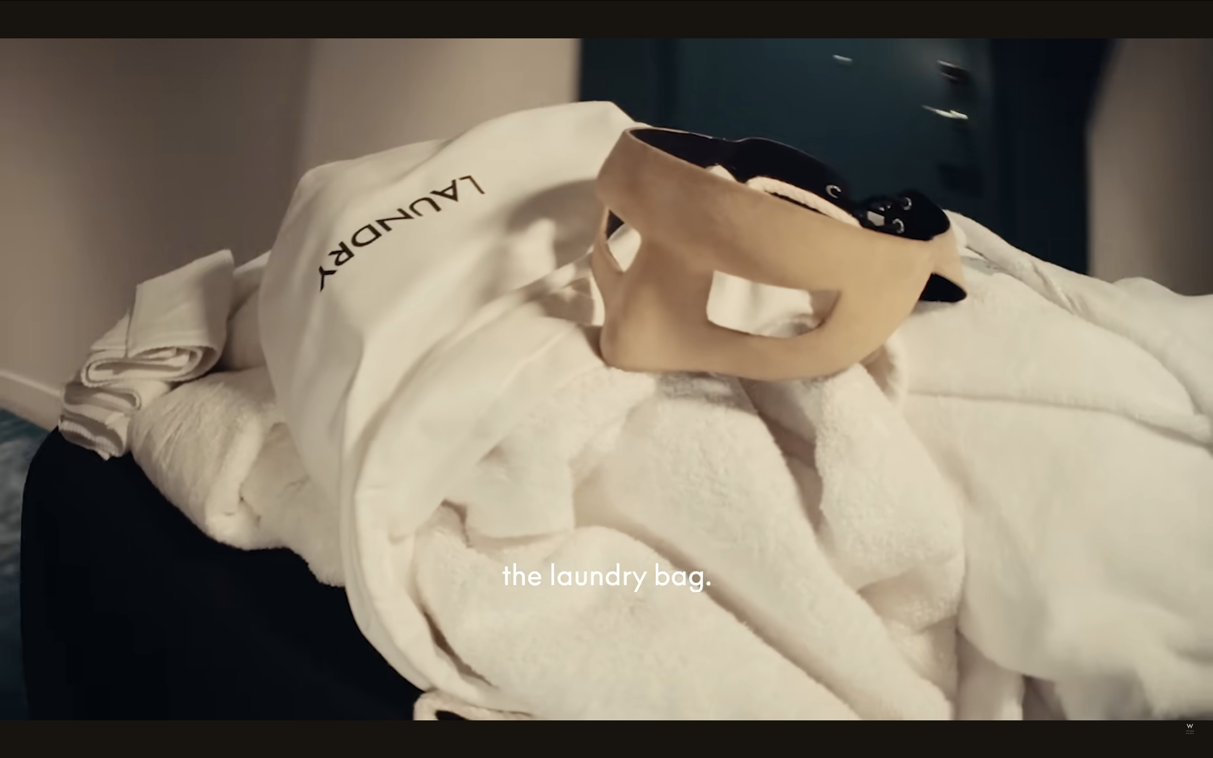 A laundry bag, a towel, and a wooden handle are placed on a bed with a white bedspread.