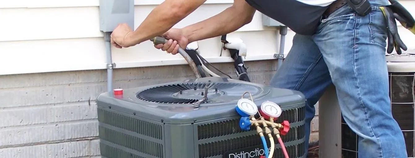 A technician repairing an air conditioning unit outside a building, using a pressure gauge and tools.