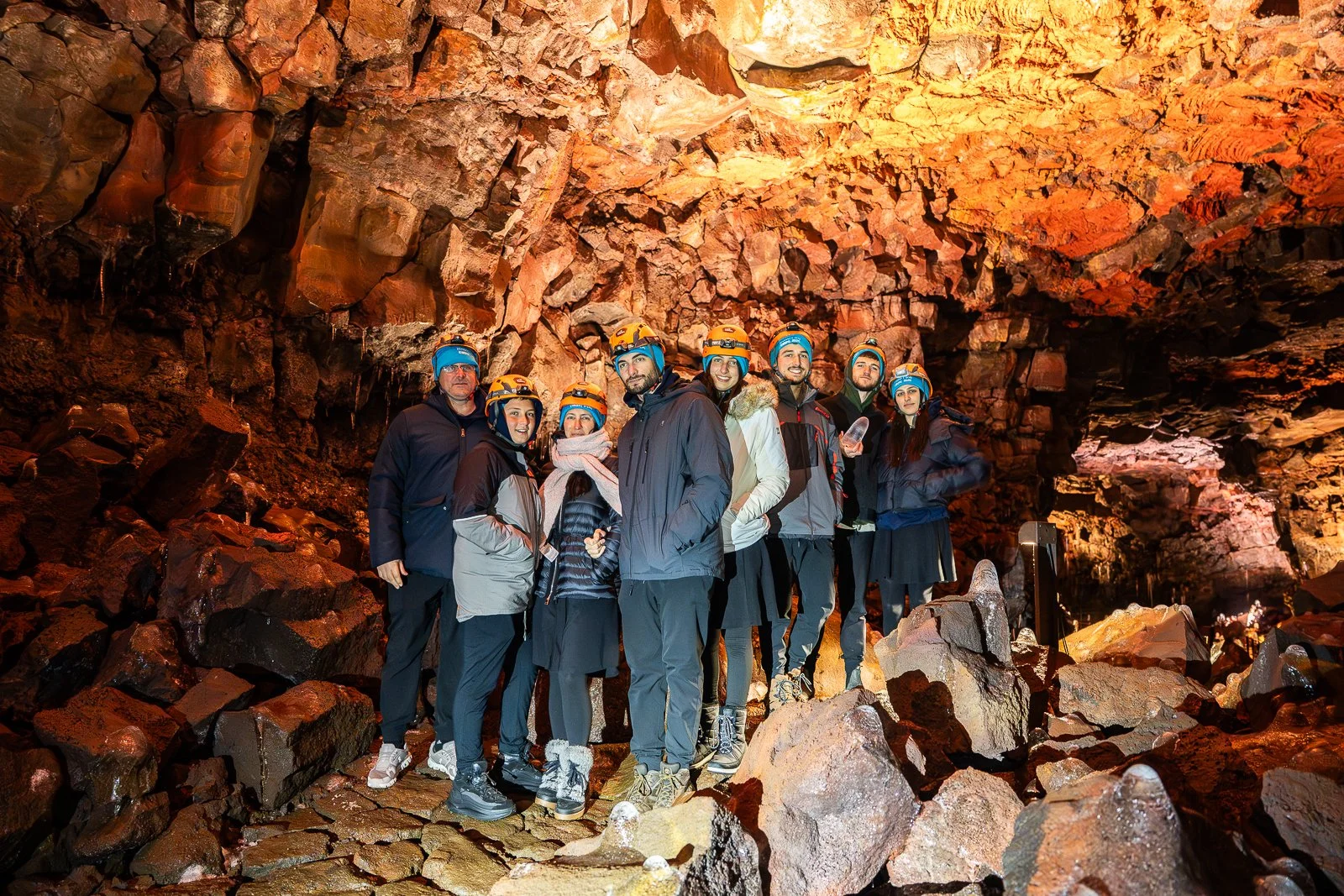 Group of people wearing helmets and outdoor gear inside a cave with rocky walls and ceiling.