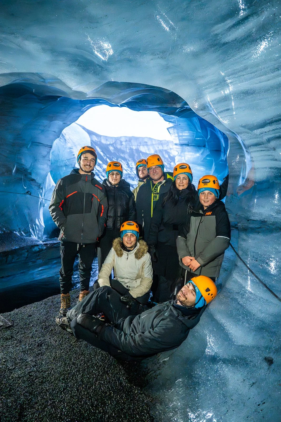 Group of people wearing helmets inside an ice cave, posing for a photo.