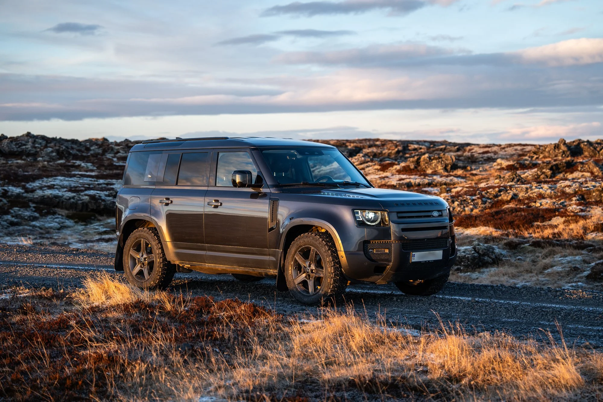 A black Range Rover SUV parked on a gravel road in a rugged, rocky landscape during sunset or sunrise with a partly cloudy sky.
