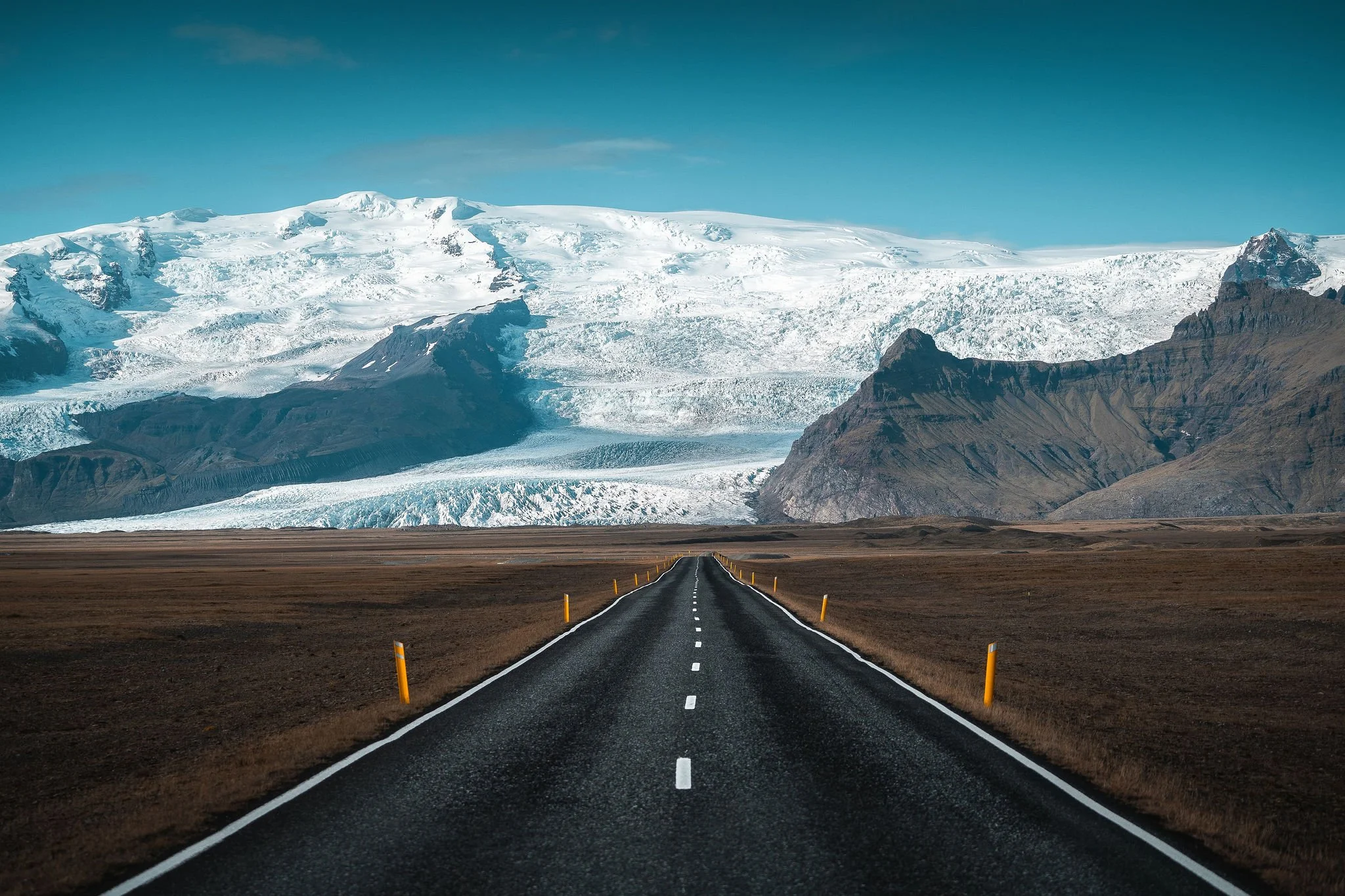 An empty Icelandic road leading towards a vast glacier