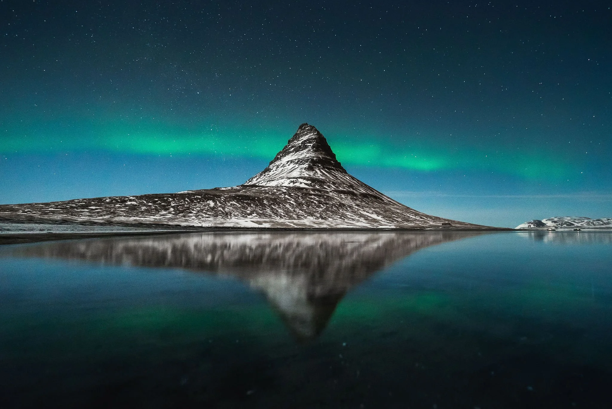 Kirkjufell Mountain with Northern Lights reflecting in the water at night.