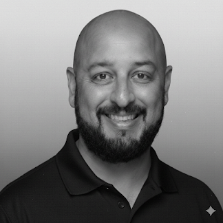 Black and white portrait of a smiling man with a beard, bald head, wearing a collared shirt.