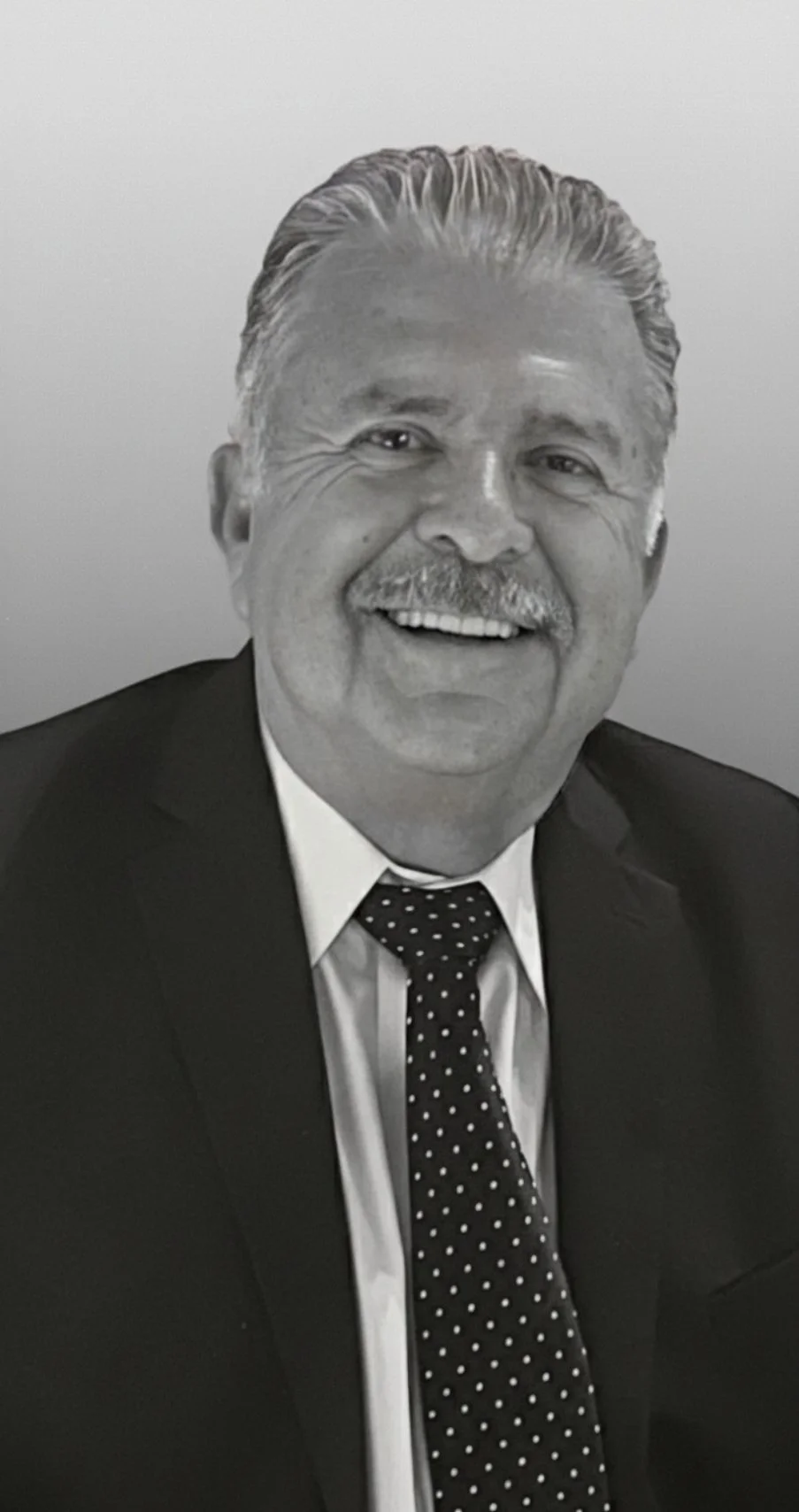 Black and white portrait of a smiling man with a mustache, wearing a suit and polka dot tie.