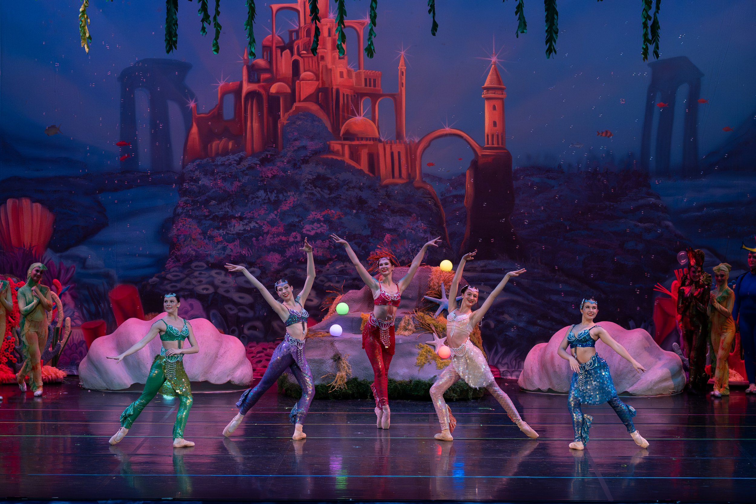 Ballet dancers performing on a stage with an undersea theme, featuring a backdrop of colorful coral and a castle living under the ocean.