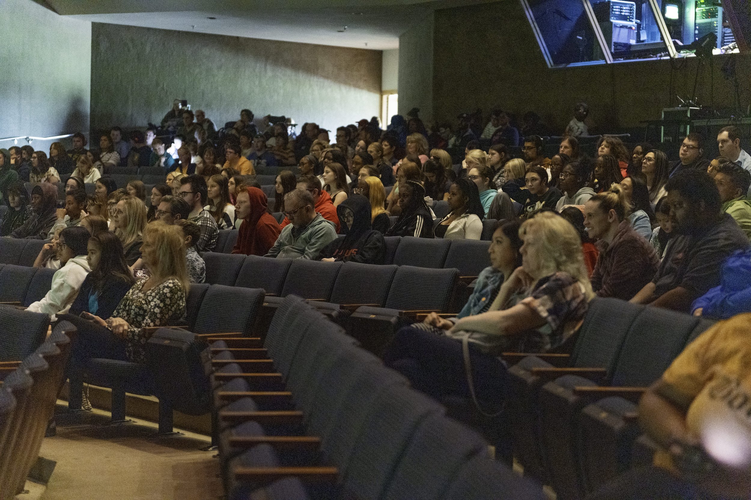 A large audience seated in rows of theater chairs, attending a presentation or performance in a conference or auditorium setting.