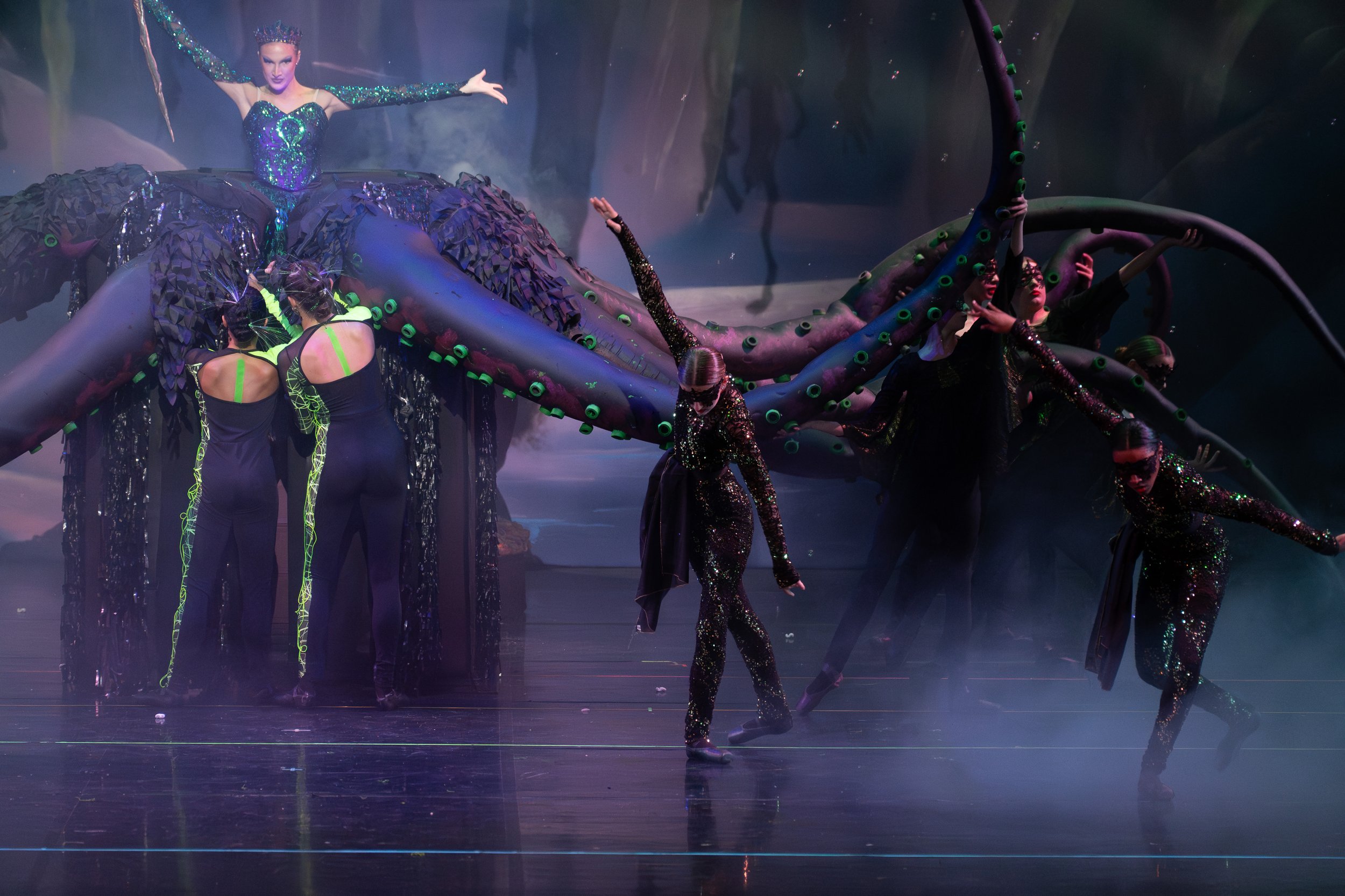 A theatrical stage performance with performers dressed in black and neon green, and a large, colorful, dragon-like puppet.