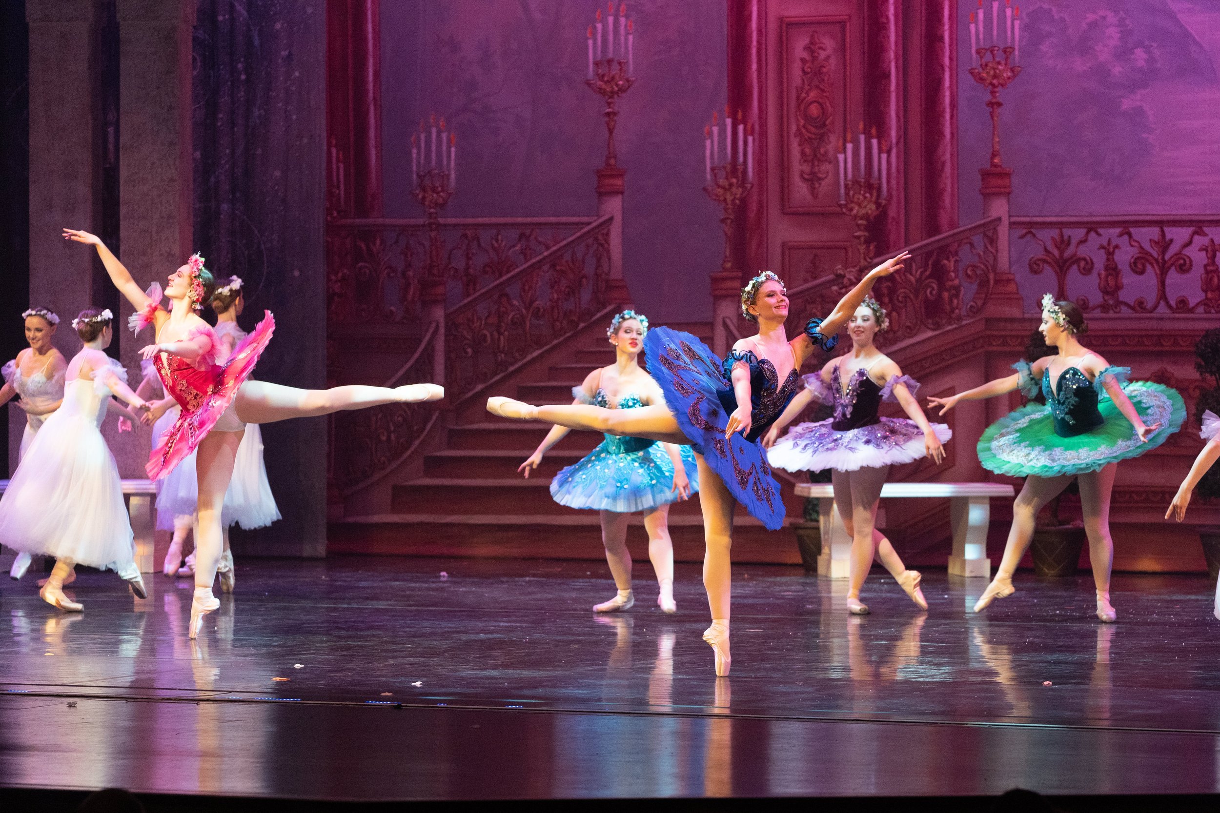 Ballet dancers performing on stage, dressed in colorful tutus, with ornate castle-like background.