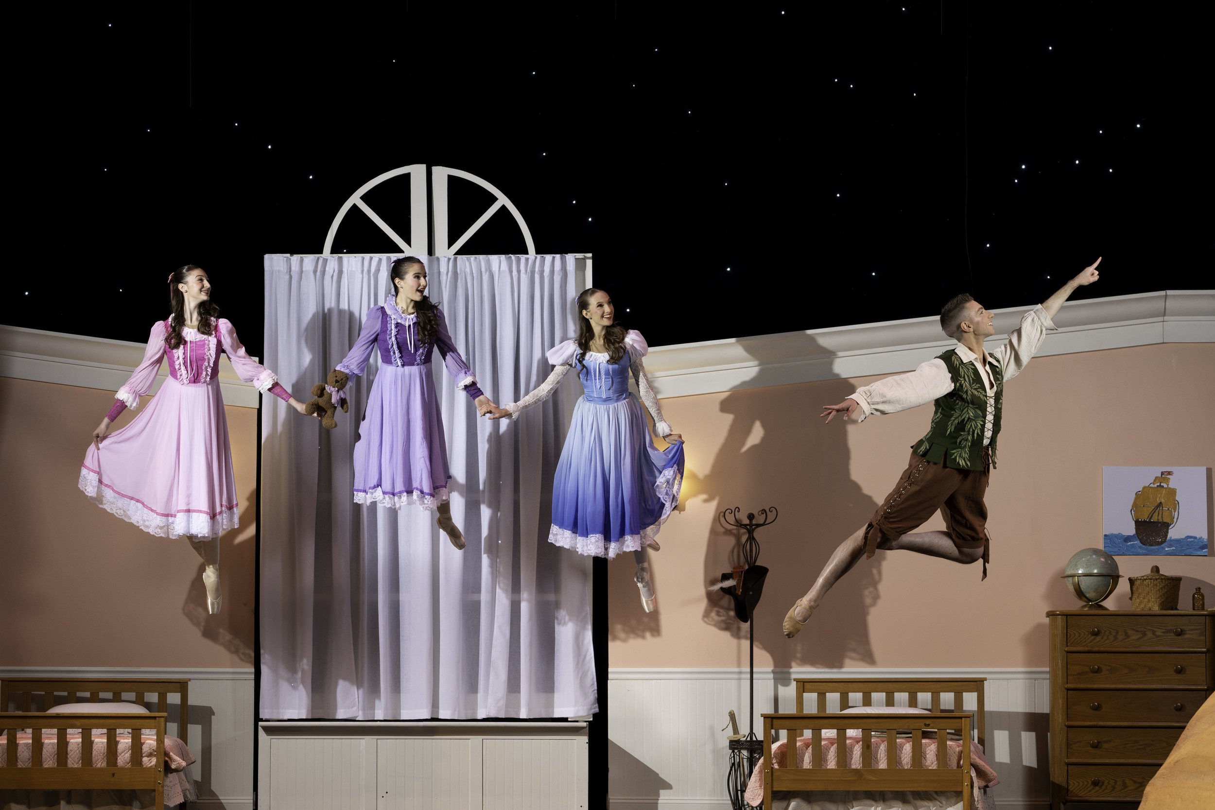 Five ballet dancers, four women in pastel dresses and one man in historical costume, performing on a stage with a bedroom set and a starry night backdrop.