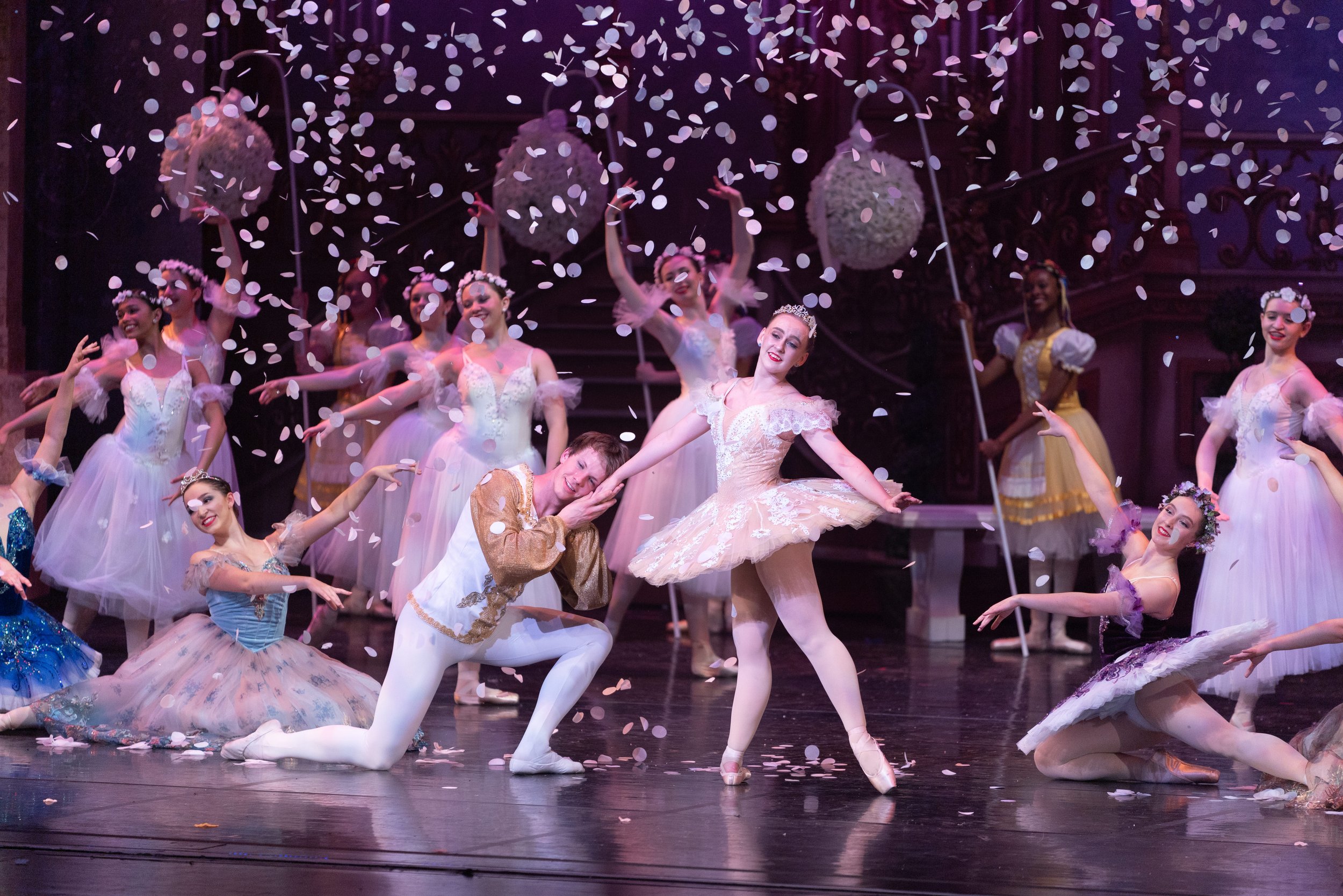 Ballet dancers performing on stage with white confetti falling around them, dressed in colorful costumes and ballet tutus.
