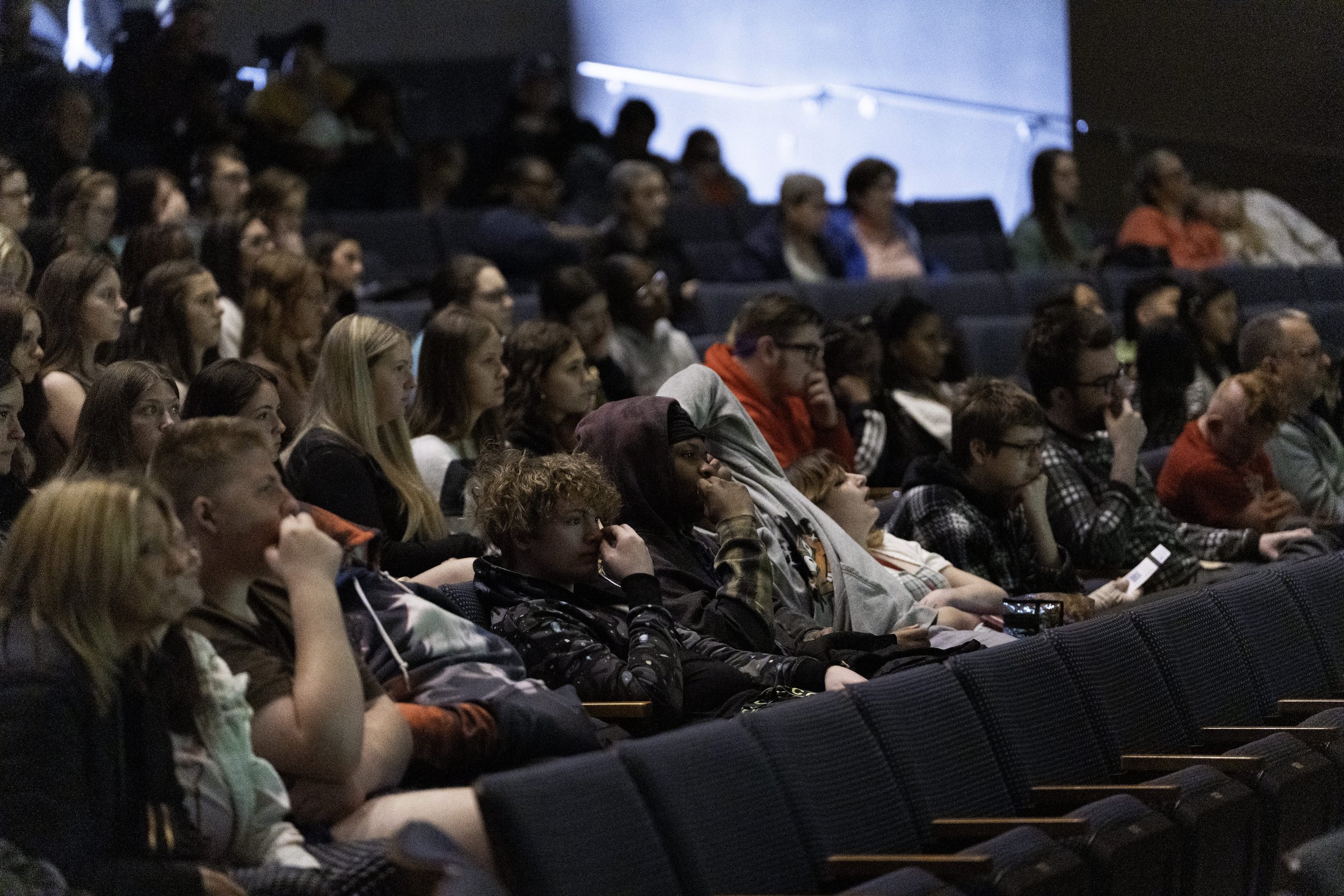 Audience seated in a dark auditorium, watching a presentation or performance.