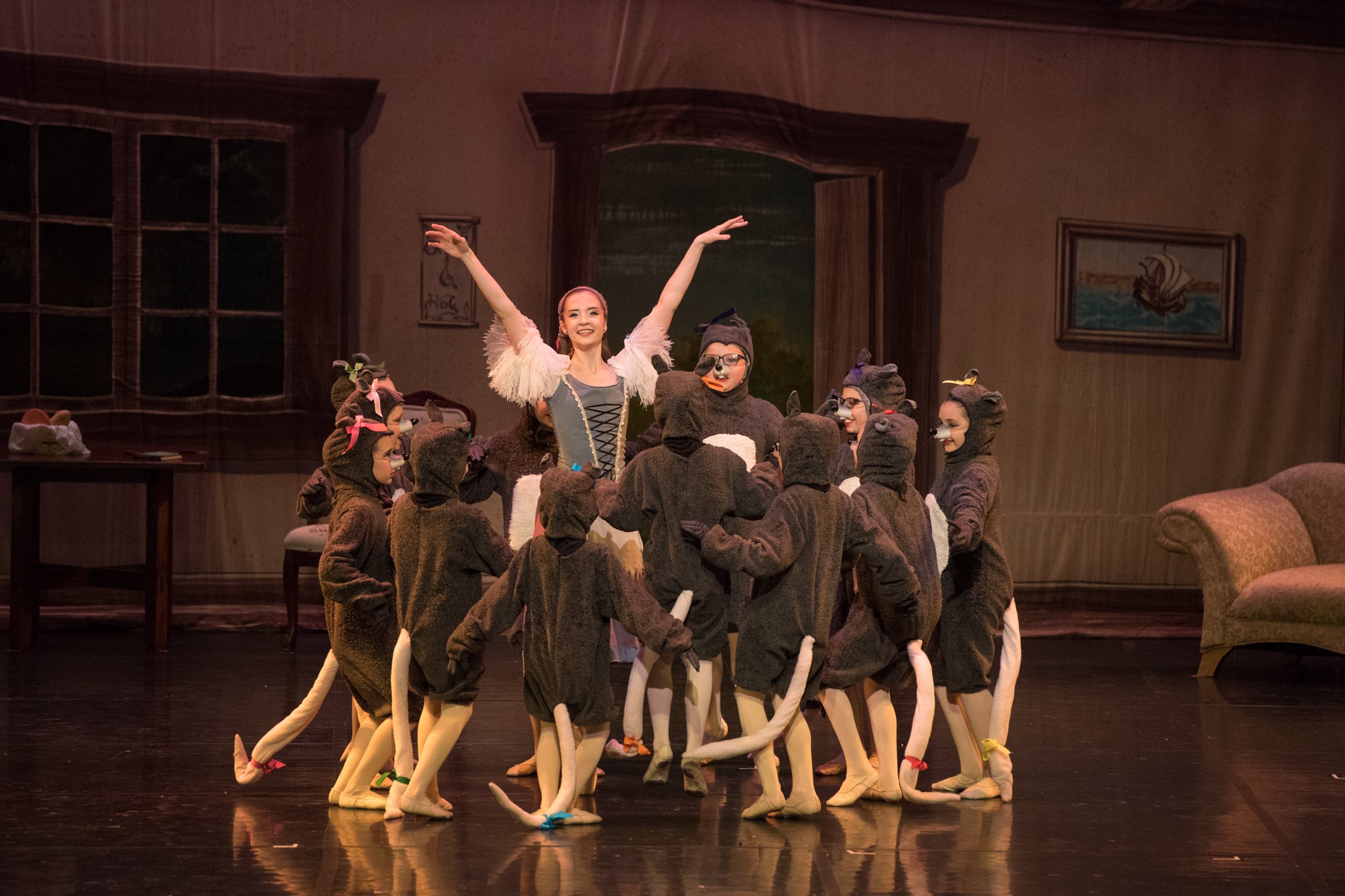 A woman in a costume performing on stage with children dressed as mice surrounding her.