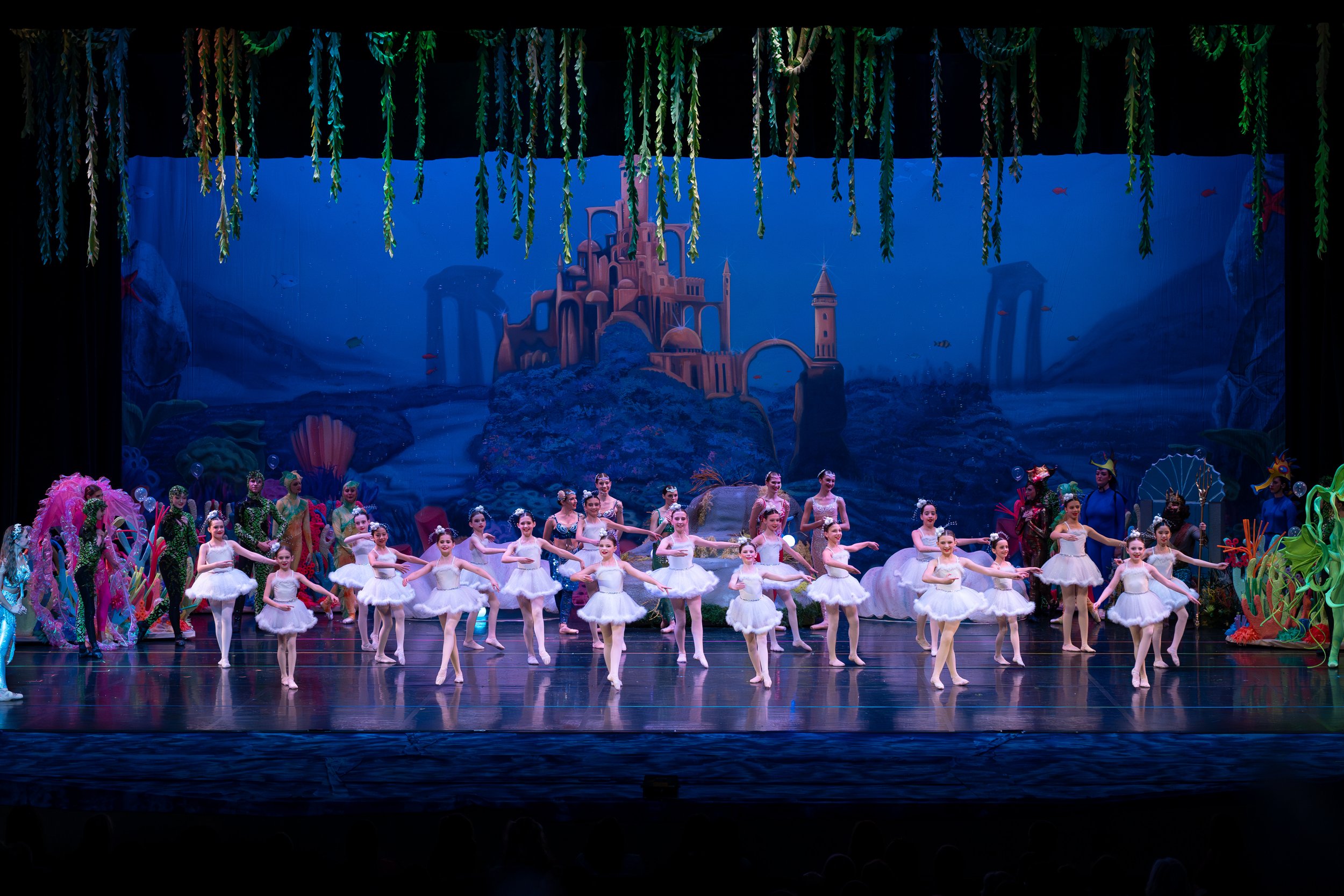 Ballet dancers performing on stage with a colorful ocean-themed backdrop featuring a castle and sea creatures.