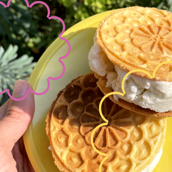 Close-up of a yellow plate holding three ice cream sandwiches with cookie wafers and vanilla ice cream, held by a hand outdoors with greenery in the background.