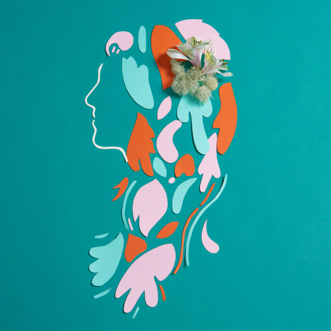 A wall art piece depicting a stylized profile of a woman's face and upper body made from colorful abstract shapes. A bouquet of real flowers is arranged on top of the artwork, adding a three-dimensional element.