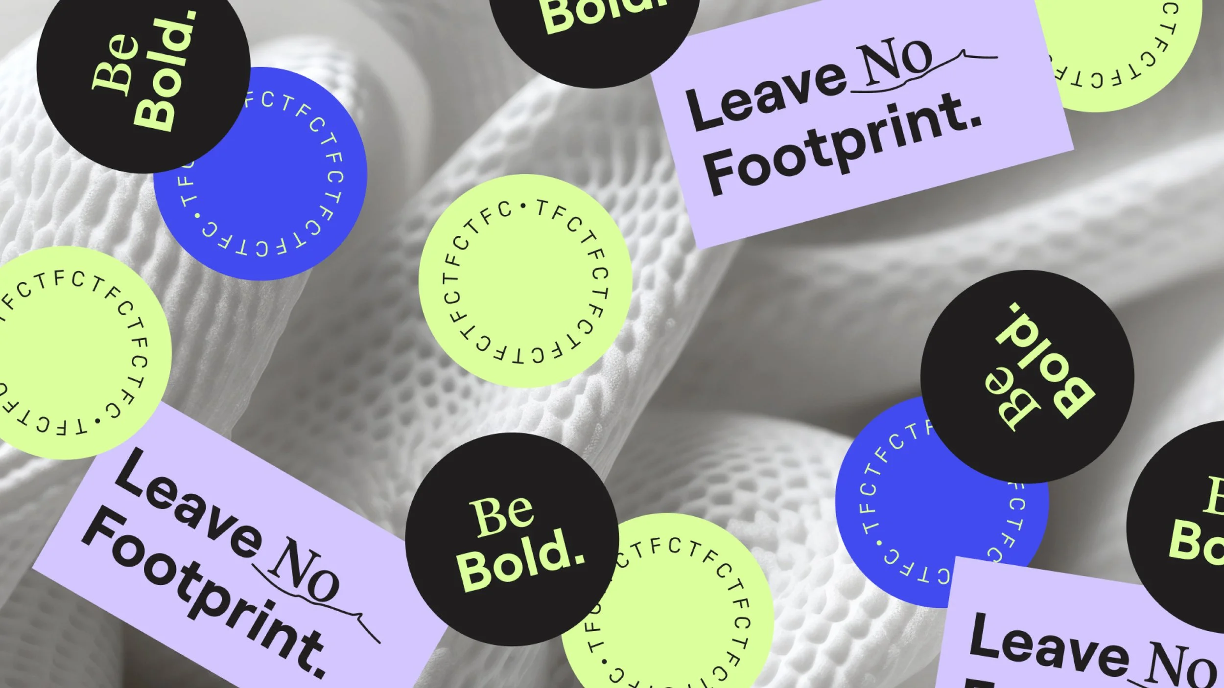 Close-up of white fabric with colorful circular and rectangular stickers overlaying that contain motivational phrases such as "Be Bold," "Be Bold!" and "Leave No Footprint".