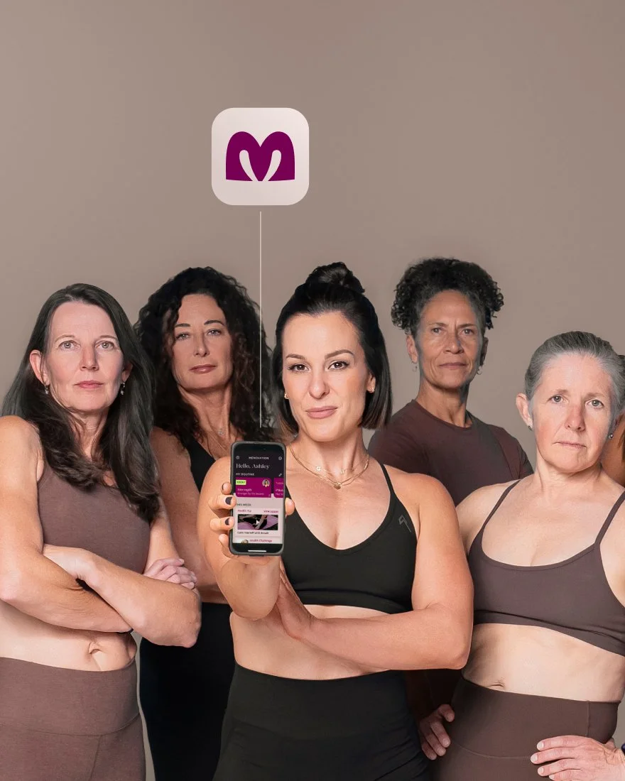 Group of five women in sports bras standing together, one holding a smartphone displaying an app with a purple logo, against a plain background.