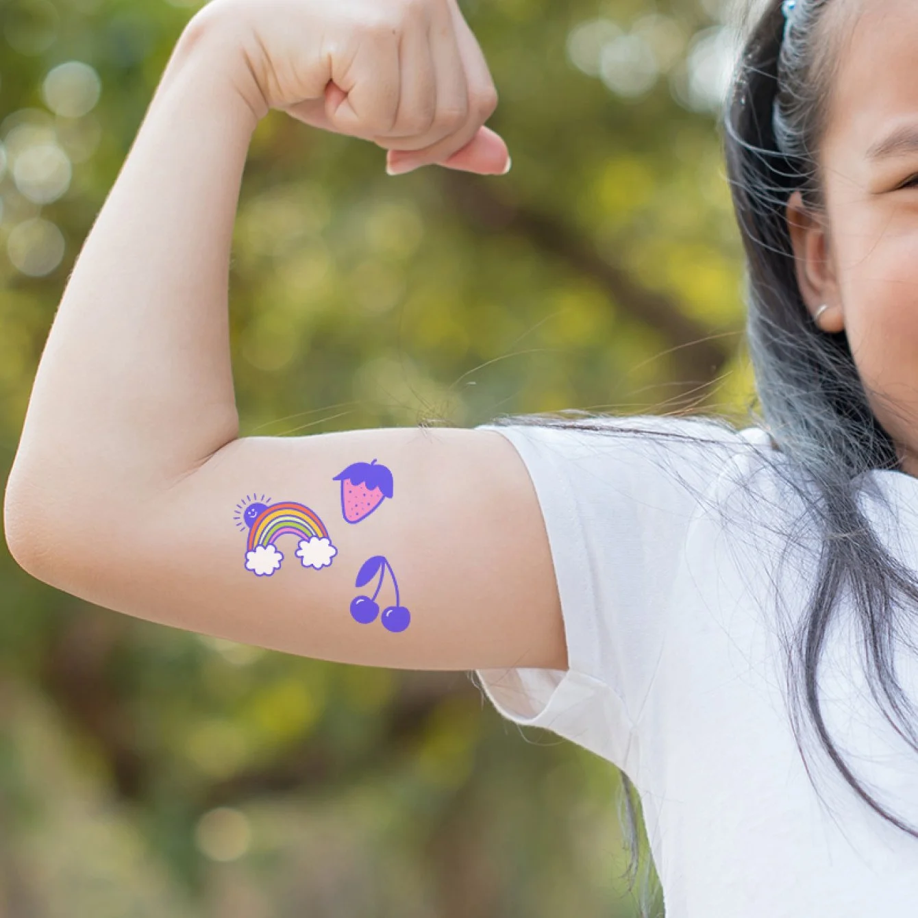 A girl showing her arm with rainbow, strawberry, and cherry temporary tattoos.