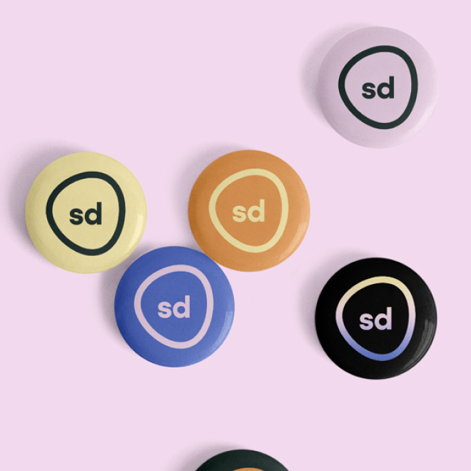 Close-up of five colorful round buttons with 'sd' logo on a pink background.