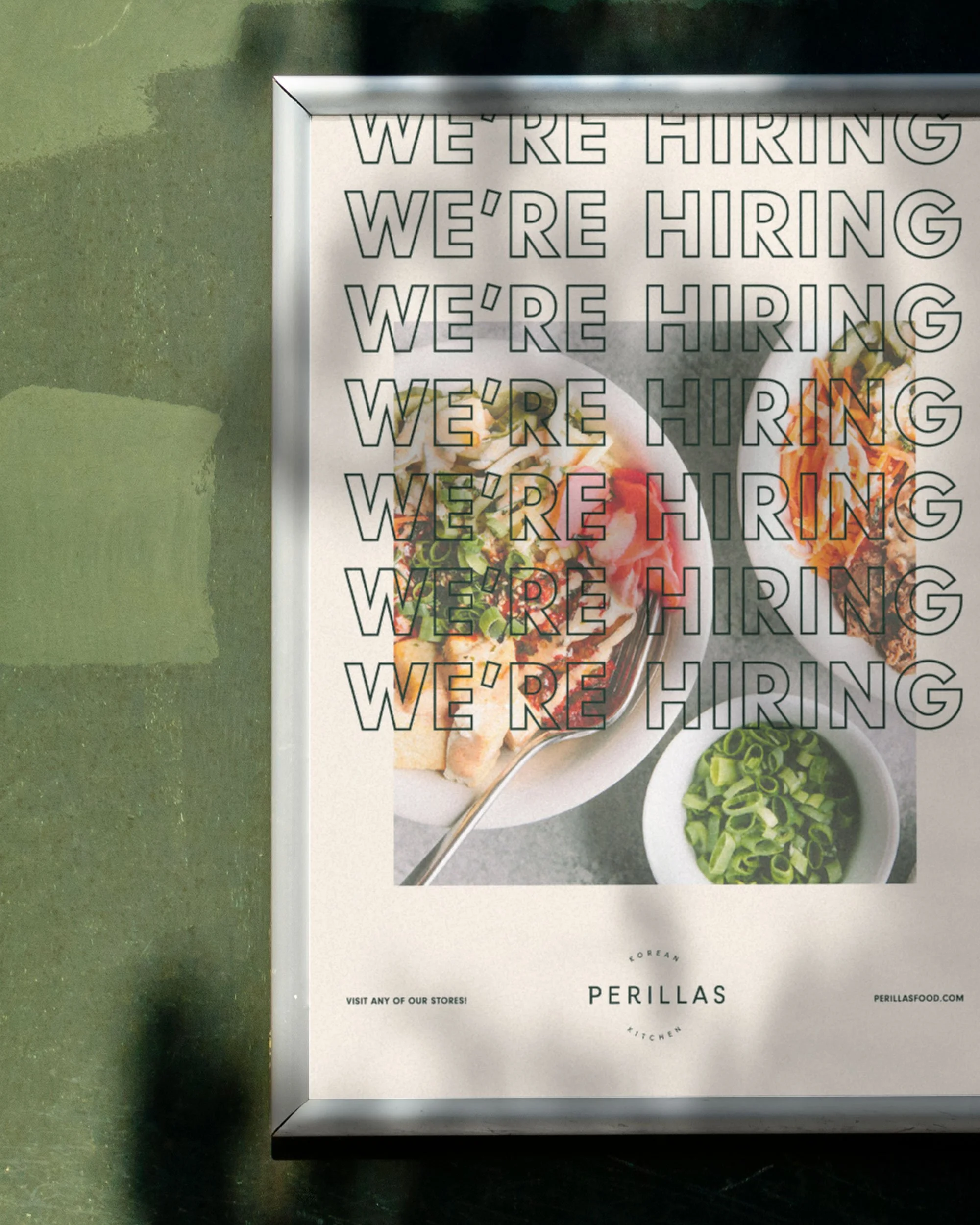A food menu sign with the words 'WE'RE HIRING' repeated throughout, placed on a green surface, showcasing a dish with vegetables and a bowl of chopped green onions at the bottom, with the restaurant name 'PERILLAS' at the bottom.