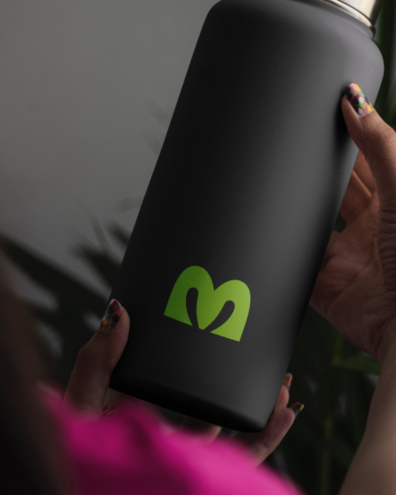 Person holding a black travel mug with a green logo of a stylized arch and the letter 'M'.
