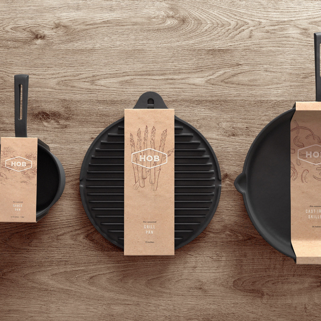 Three black cast iron grilling pans on a light wooden surface, each with a paper sleeve displaying the HOB brand logo and illustrations, indicating they are grill pans.