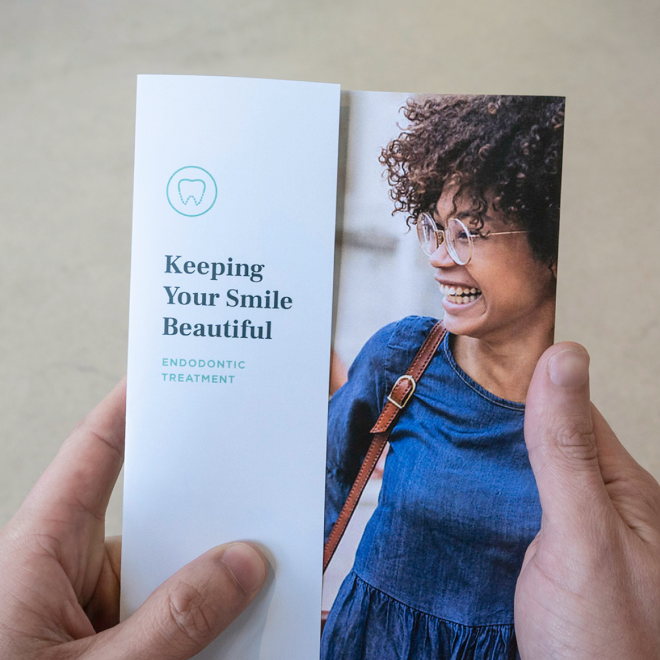 A person holding a brochure for endodontic treatment with a smiling woman on the cover.