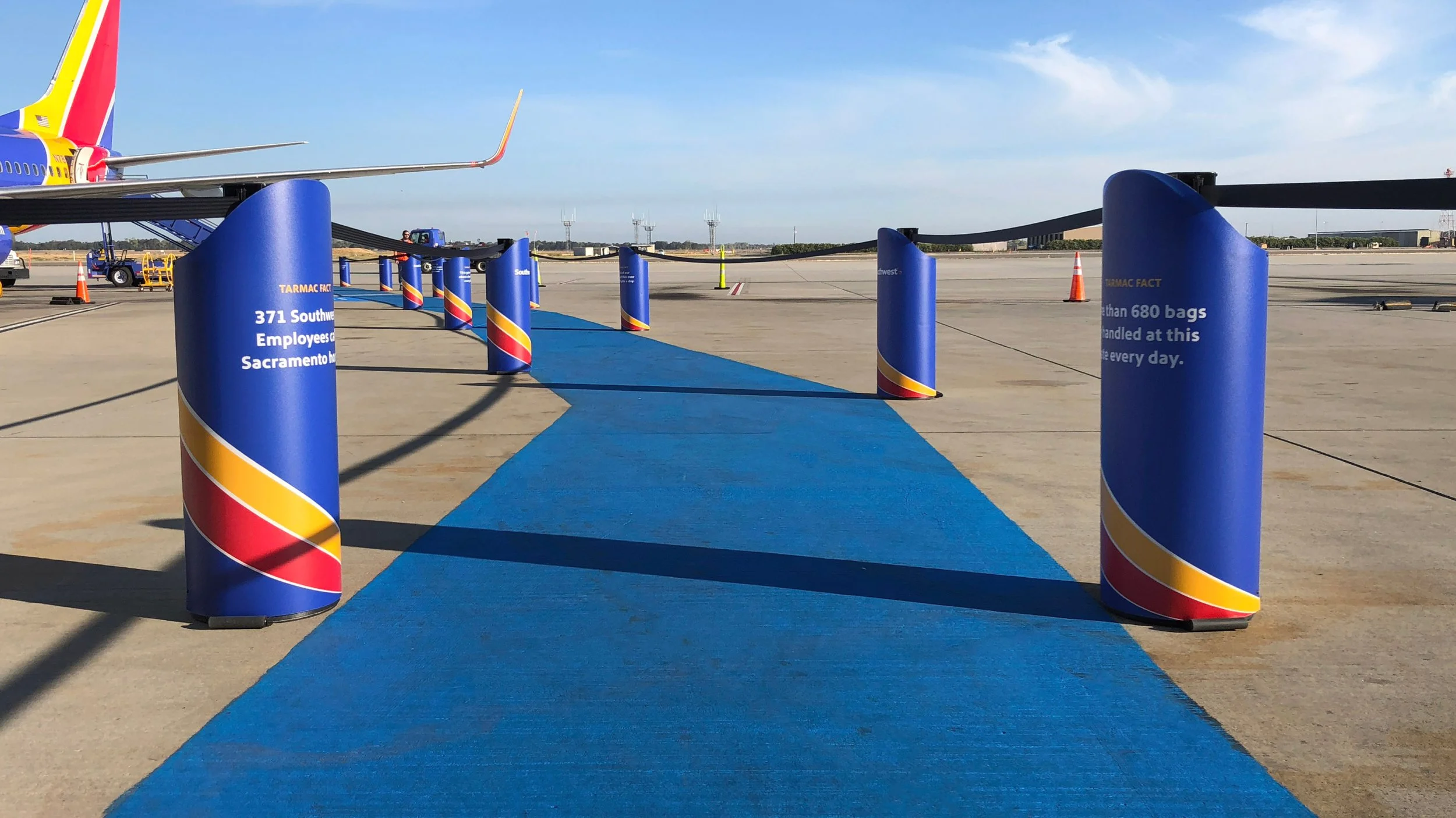 Blue pathway with safety posts on the sides leading to an airplane on the tarmac at an airport.