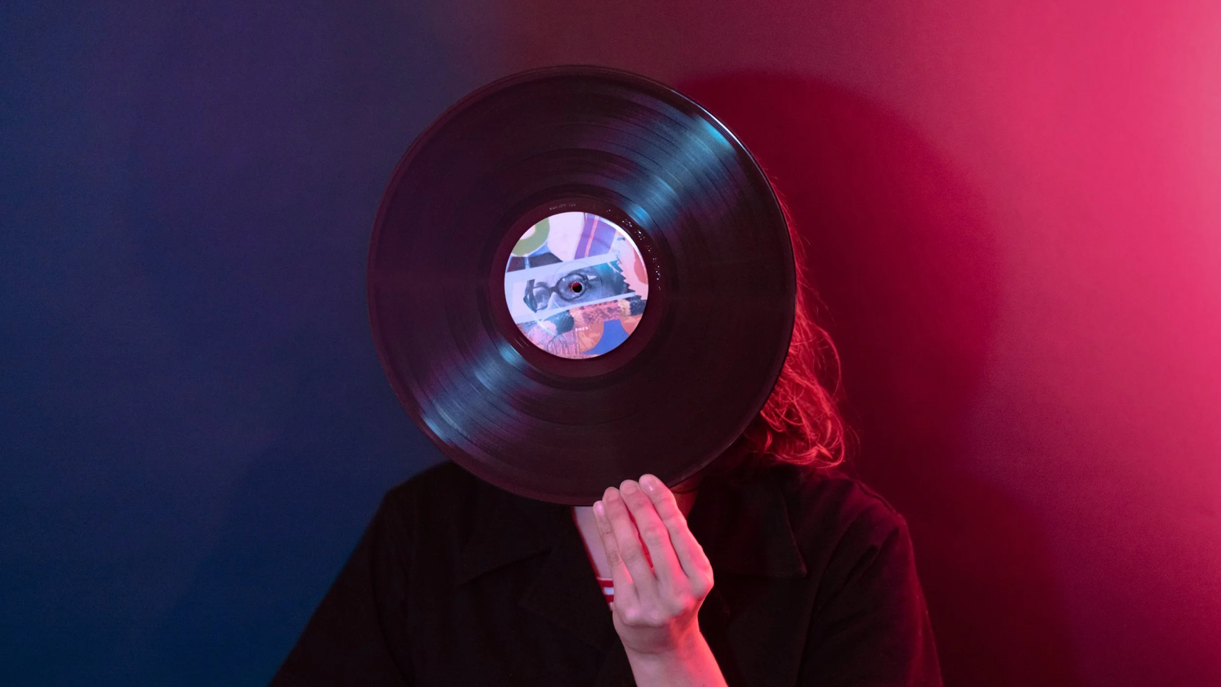 Person holding a vinyl record in front of face, colorful background with red and blue lighting.