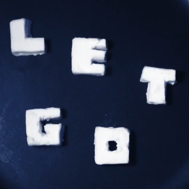 White letter tiles spelling out "LET GO" in butter on a dark surface.