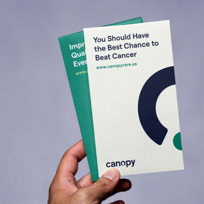 A hand holding two brochures about cancer prevention and. early detection, with a plain gray background.