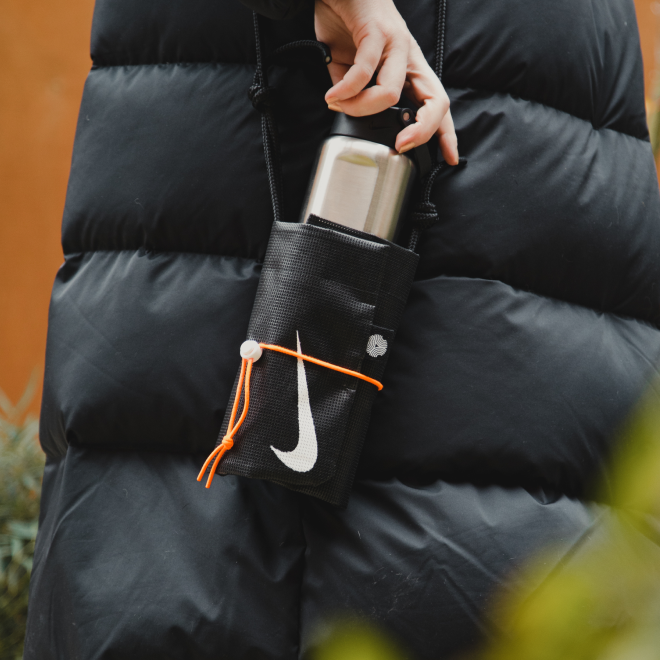 Person wearing a black puffer jacket with a Nike-branded water bottle in a side pocket.