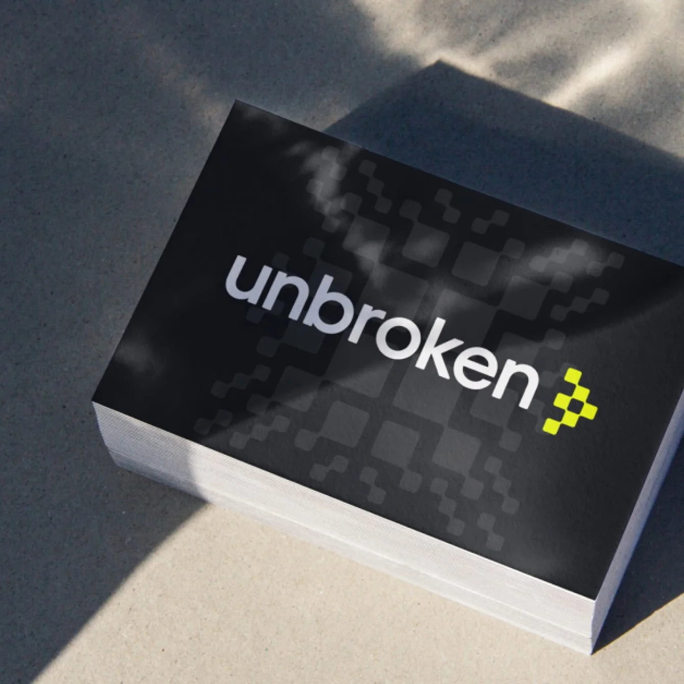A stack of business cards with the title 'unbroken' in white text and a yellow number three on the cover, resting on a light-colored surface with shadows.